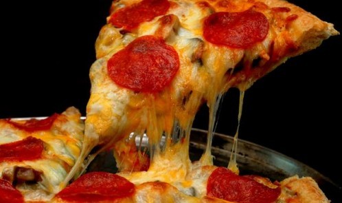 Slice of pepperoni pizza being removed from whole pizza with tomatoes in background. Isolated on black background.